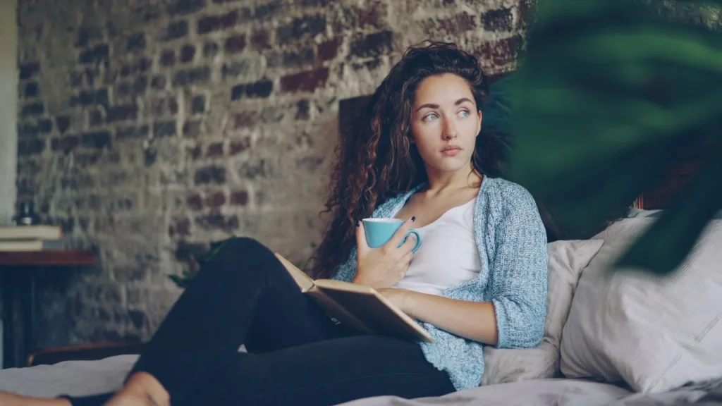 A young woman enjoys a quiet moment with coffee and a book at home.